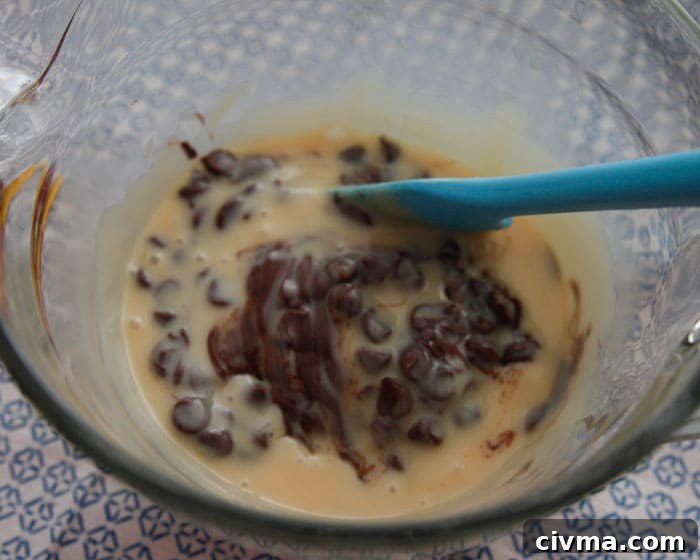 3 minute fudge A blue spatula stirs sweetened condensed milk and partially melted chocolate chips in a glass bowl.