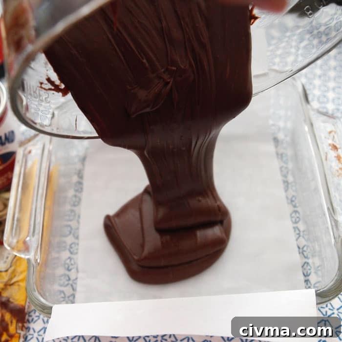 3 minute fudge Three minute fudge mixture is poured from the glass bowl into a parchment paper lined square glass baking pan.
