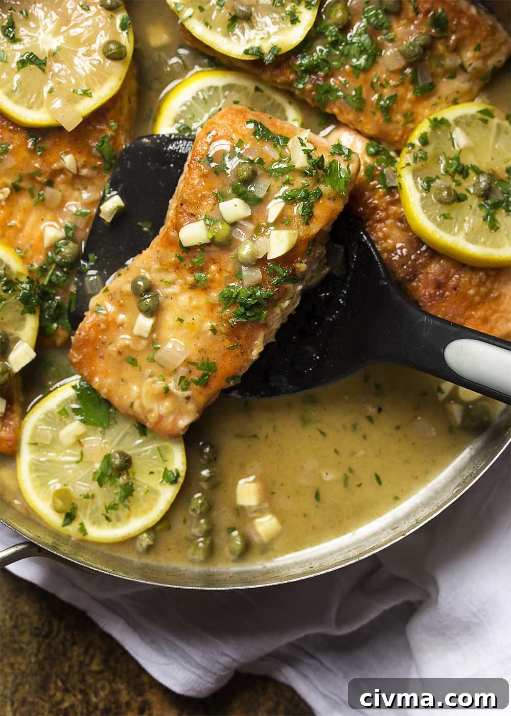 A spatula holding up a piece of salmon piccata ready to serve it onto a plate.