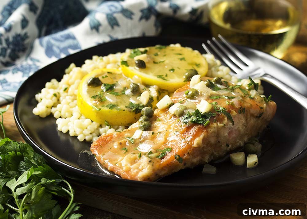 Plate with a fillet of salmon over pearl couscous all topped with a tangy lemon caper sauce.