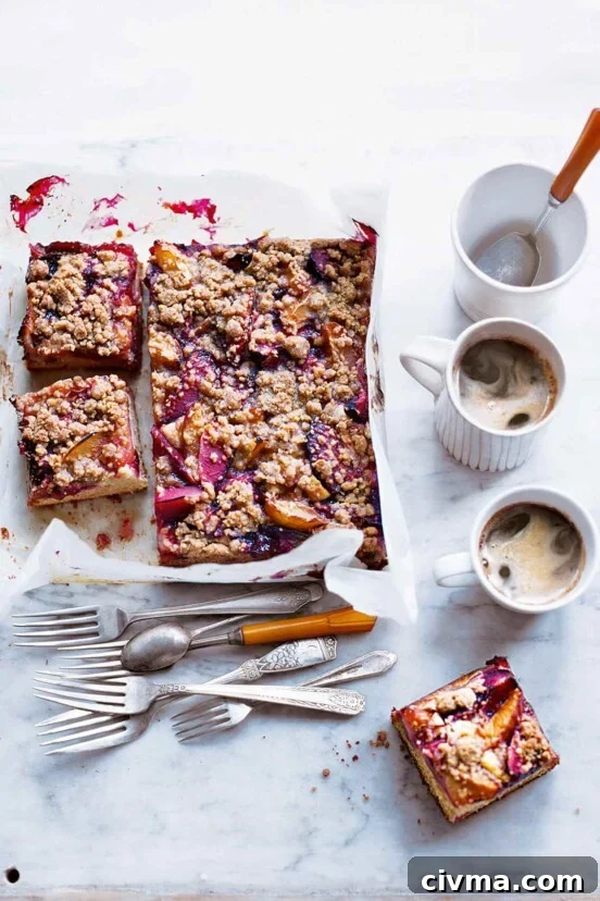 German Plum Cake Recipe 5 A plum kuchen on a sheet of parchment with three slices cut from it and a collection of forks, a spoon, and two coffee cups nearby.