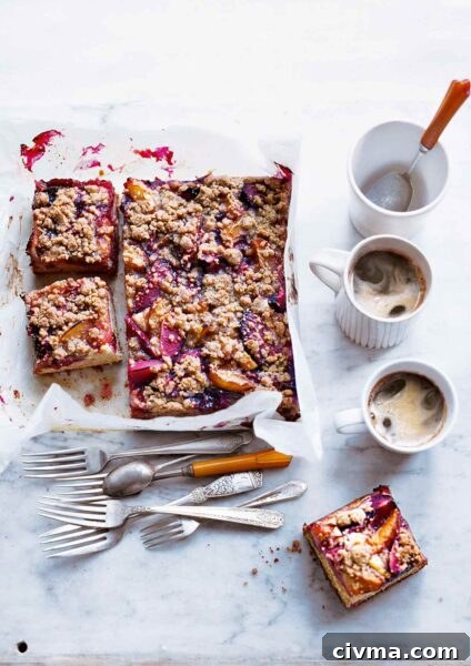 German Plum Cake Recipe 6 A plum kuchen on a sheet of parchment with three slices cut from it and a collection of forks, a spoon, and two coffee cups nearby.