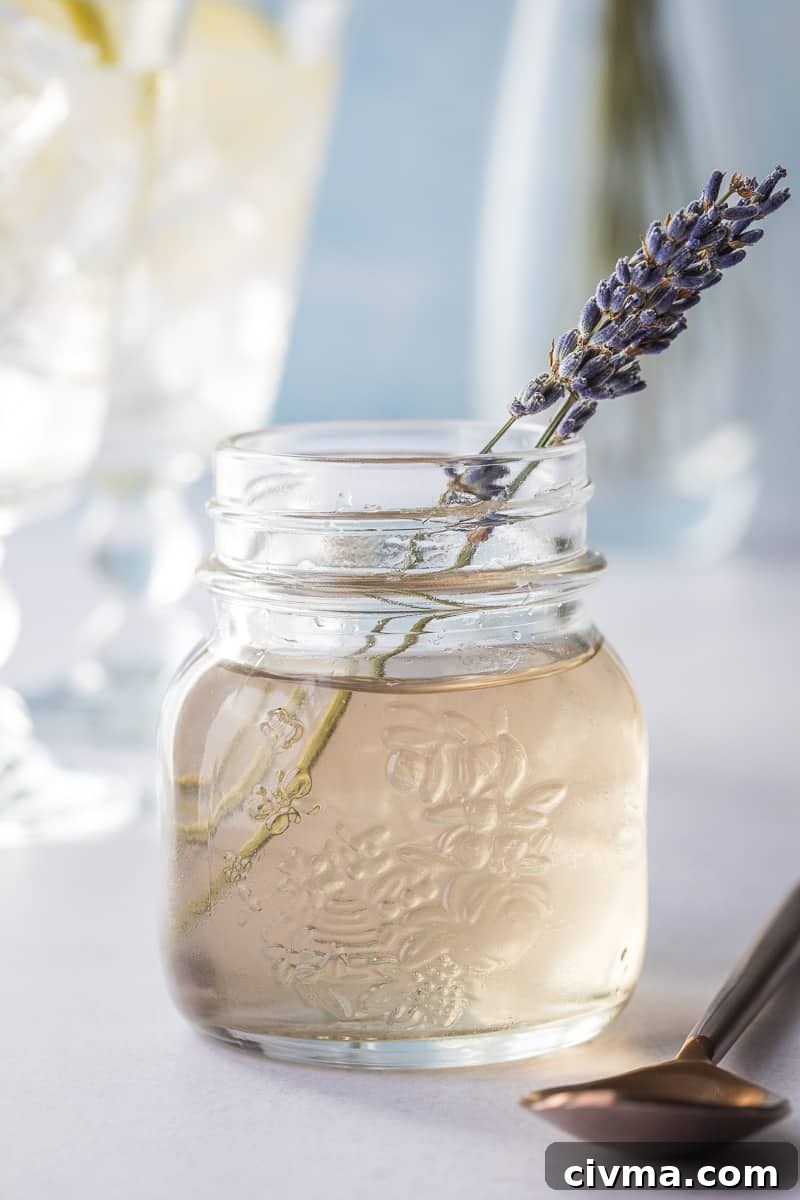 jar of lavender syrup with sprigs of lavender in front of glasses and vase.