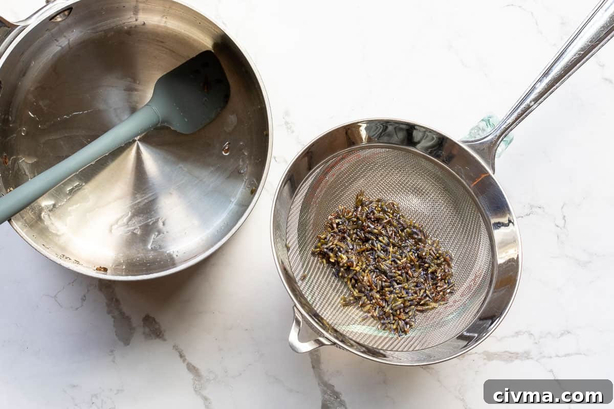 lavender buds in strainer on top of measuring cup next to saucepan with spatula.
