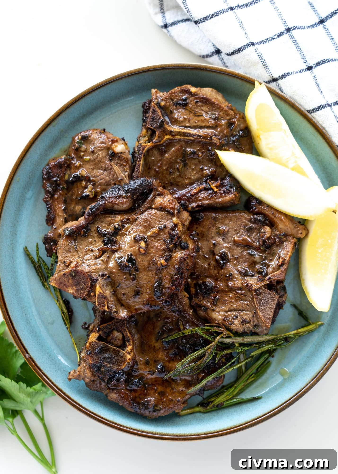 Mediterranean lamb chops seared and served on a blue plate with some lemon slices and parsley.