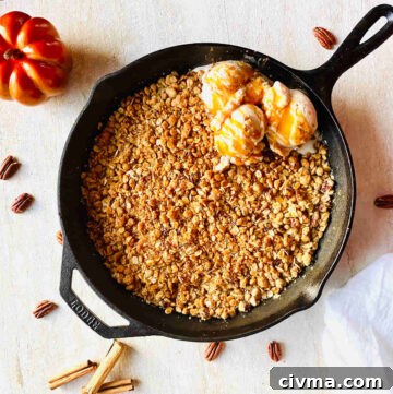cast iron skillet apple crisp with ice cream next to pecans and a pumpkin