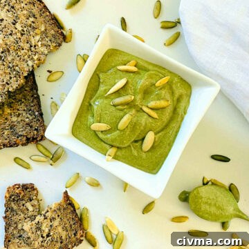 pumpkin seed butter in white dish next to spoon, bread and napkin