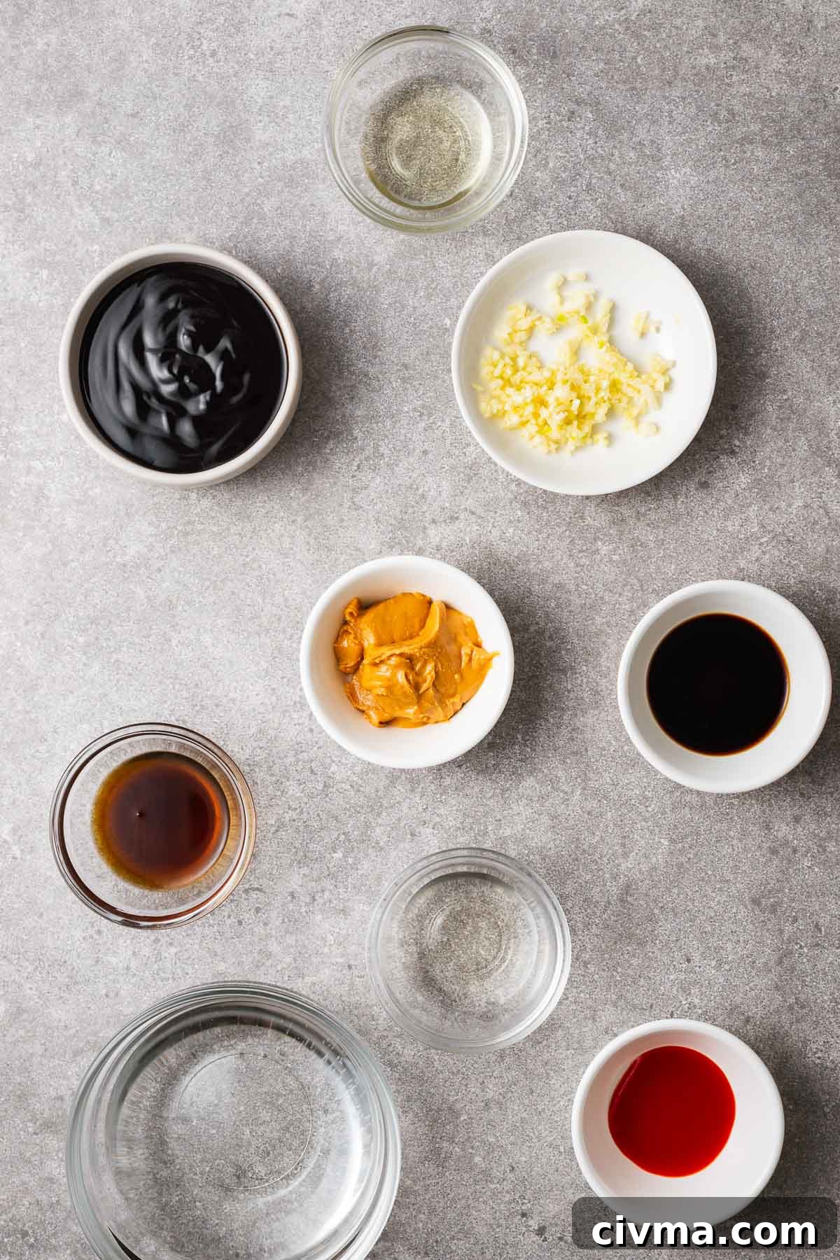Ingredients for hoisin peanut sauce arranged in small bowls including hoisin sauce, peanut butter, minced garlic, toasted sesame oil, sriracha sauce, rice vinegar and water.