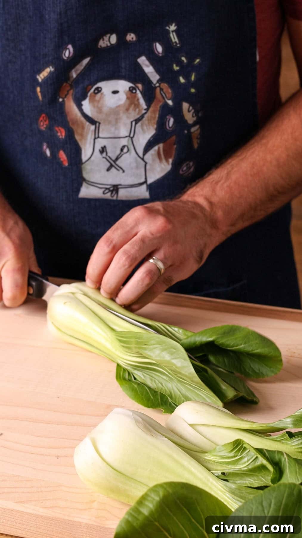 Roasted Bok Choy Recipe with Garlic and Sesame 4 Baby bok choy getting cut in half on a wooden cutting board.
