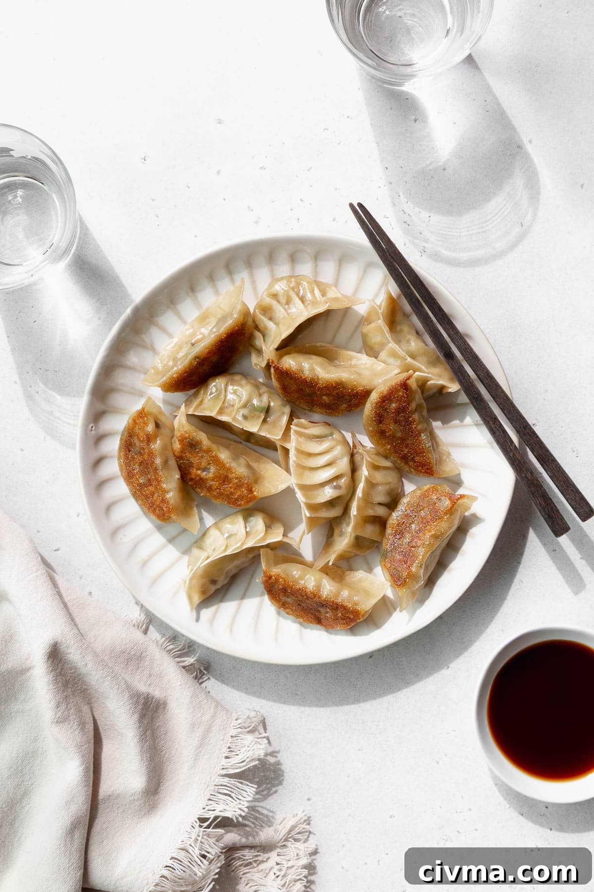 Overhead shot of vegetable gyoza on a white plate with wooden chopsticks.