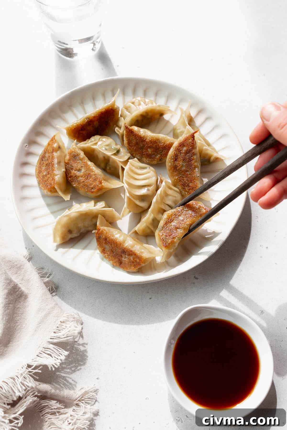 A hand holding chopsticks reaching to pick up a vegan gyoza off a plate.