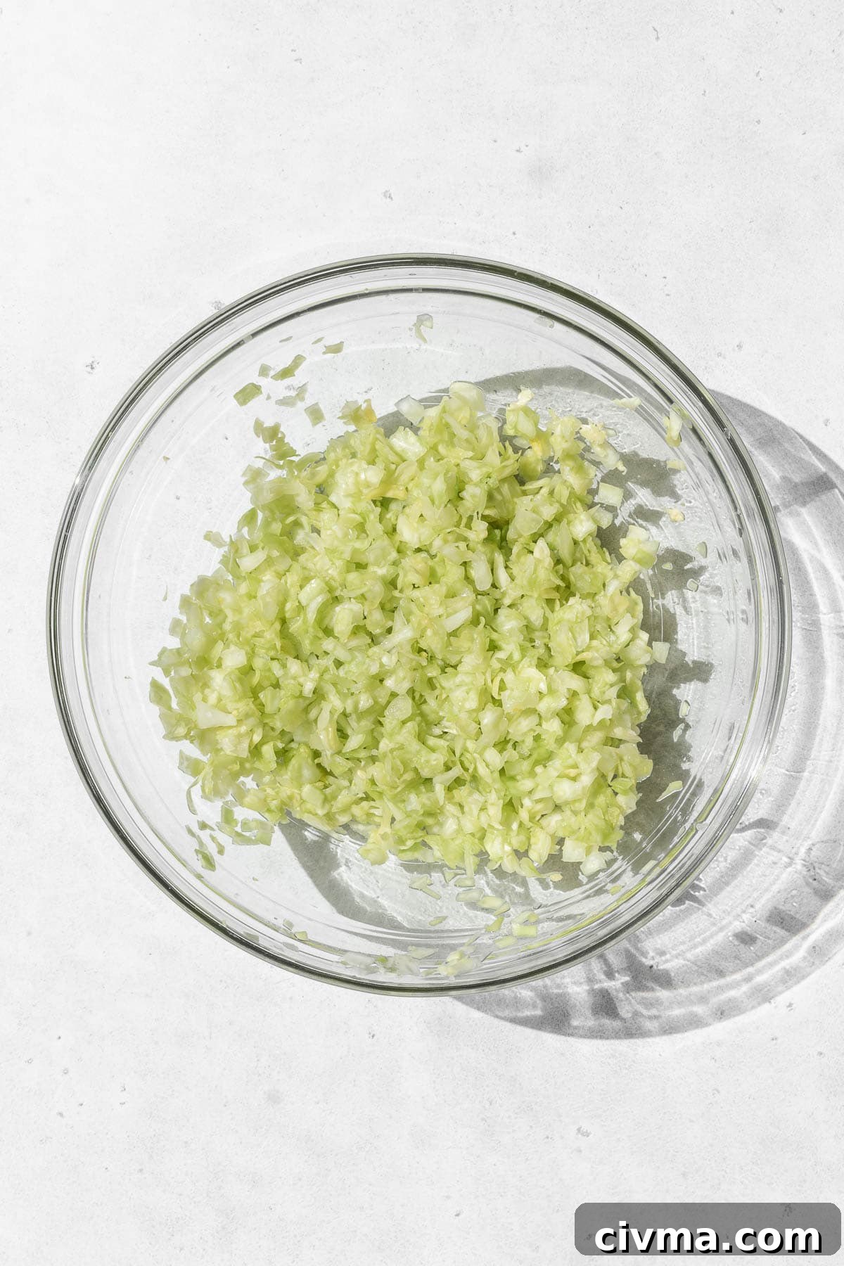 Minced cabbage in a glass bowl on a white surface.
