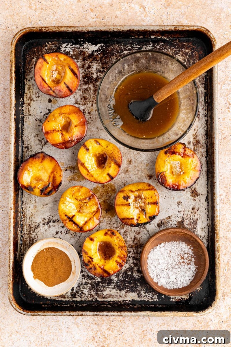 grilled peaches on a baking sheet with flaky sea salt, cinnamon and brown sugar butter on the side in bowls.