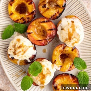 grilled peaches with scoops of ice cream on top and mint leaves for garnish on a white oval serving plate.