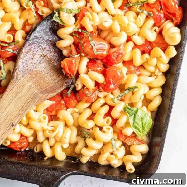 Pasta with feta and tomatoes, in a black baking dish with wooden spoon.