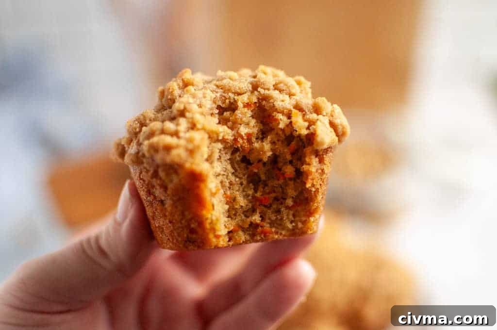 A hand holding a partially eaten Carrot Muffin with Streusel Topping, showing the moist interior.