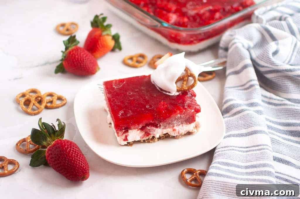 A slice of Strawberry Pretzel Salad topped with whipped cream and a pretzel sits on a white plate.