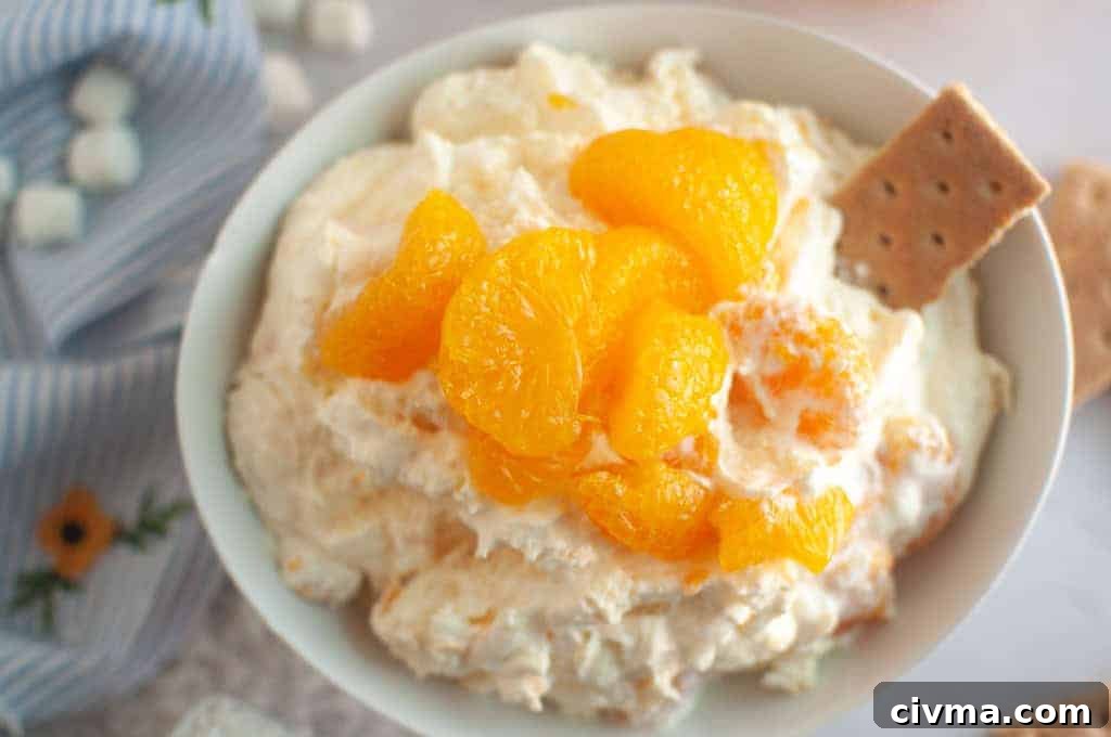Overhead shot of a white bowl filled with creamy Orange Fluff Salad, topped with mandarin oranges and served with graham crackers.