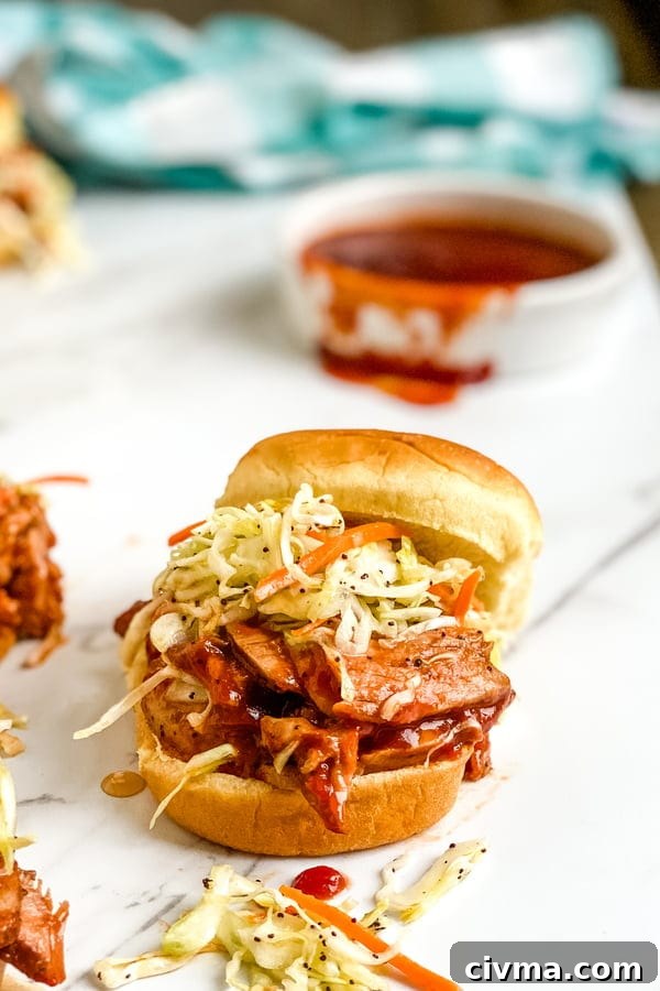 A mini bbq pork tenderloin slider with cole slaw and bbq sauce.