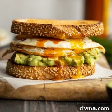 sandwich on parchment paper on chopping board with chives, hot sauce and eggs blurred in background