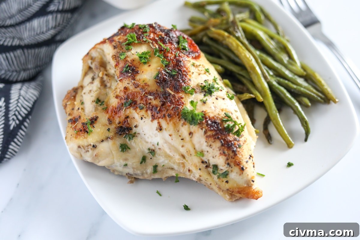 Baked italian chicken breast on a white plate with green beans on the side.