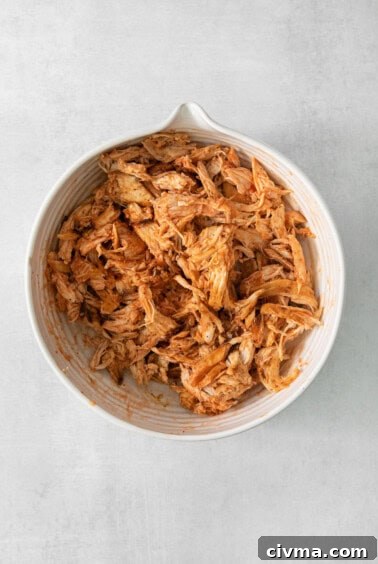 Buffalo Chicken Quesadilla Recipe 11 Shredded chicken in a white bowl on a grey background.