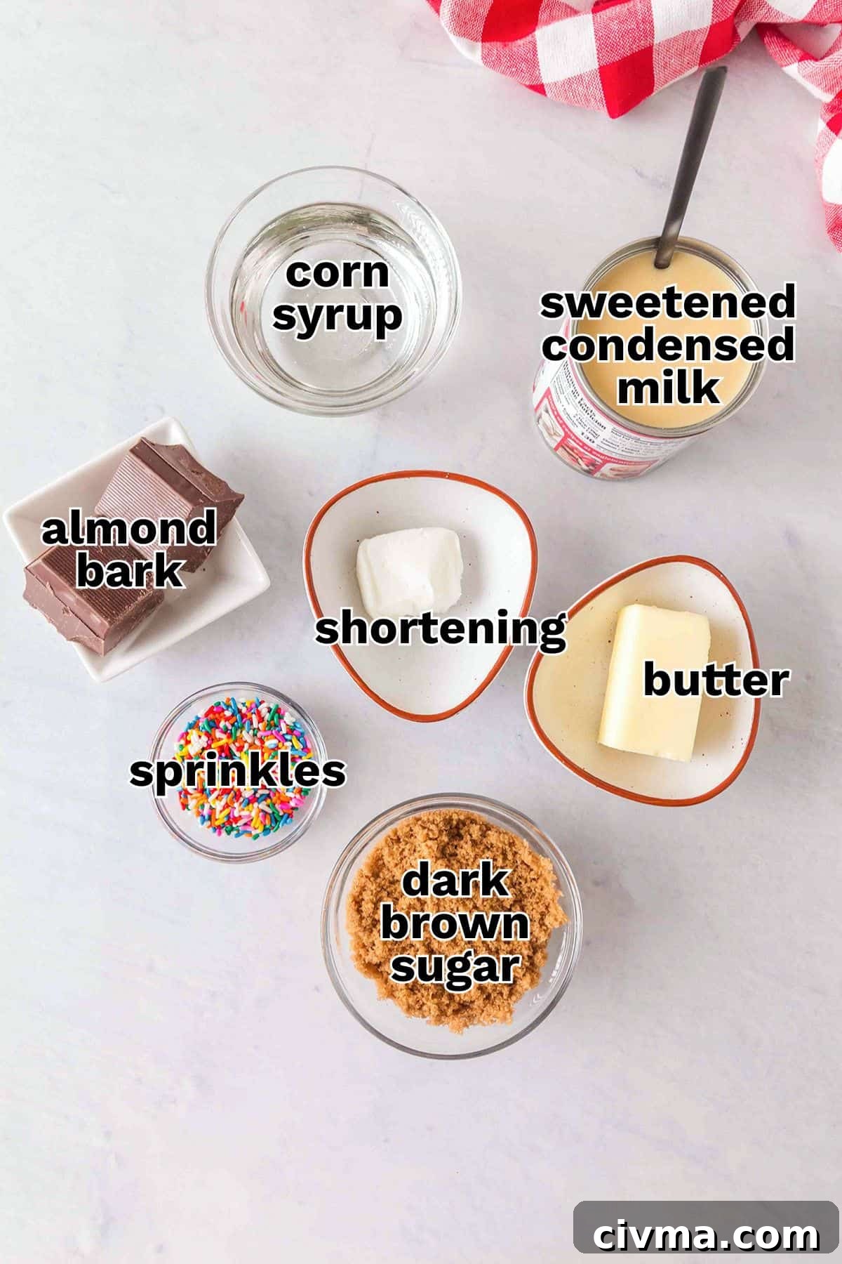 Various baking ingredients are arranged on a white surface, each labeled: corn syrup, sweetened condensed milk, almond bark, shortening, butter, sprinkles, and dark brown sugar—perfect for making Soft & Chewy Caramels.