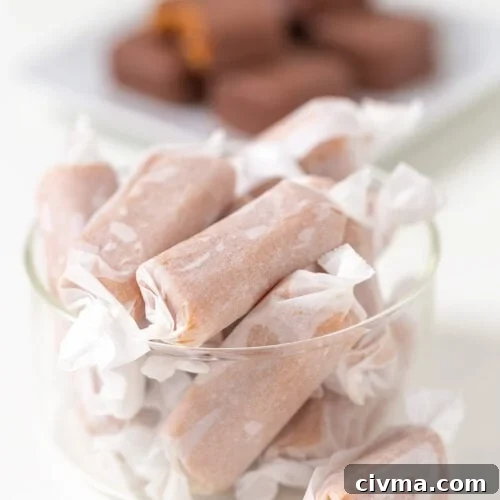 A glass bowl filled with Soft & Chewy Caramels, with a plate of chocolate-covered candies blurred in the background.