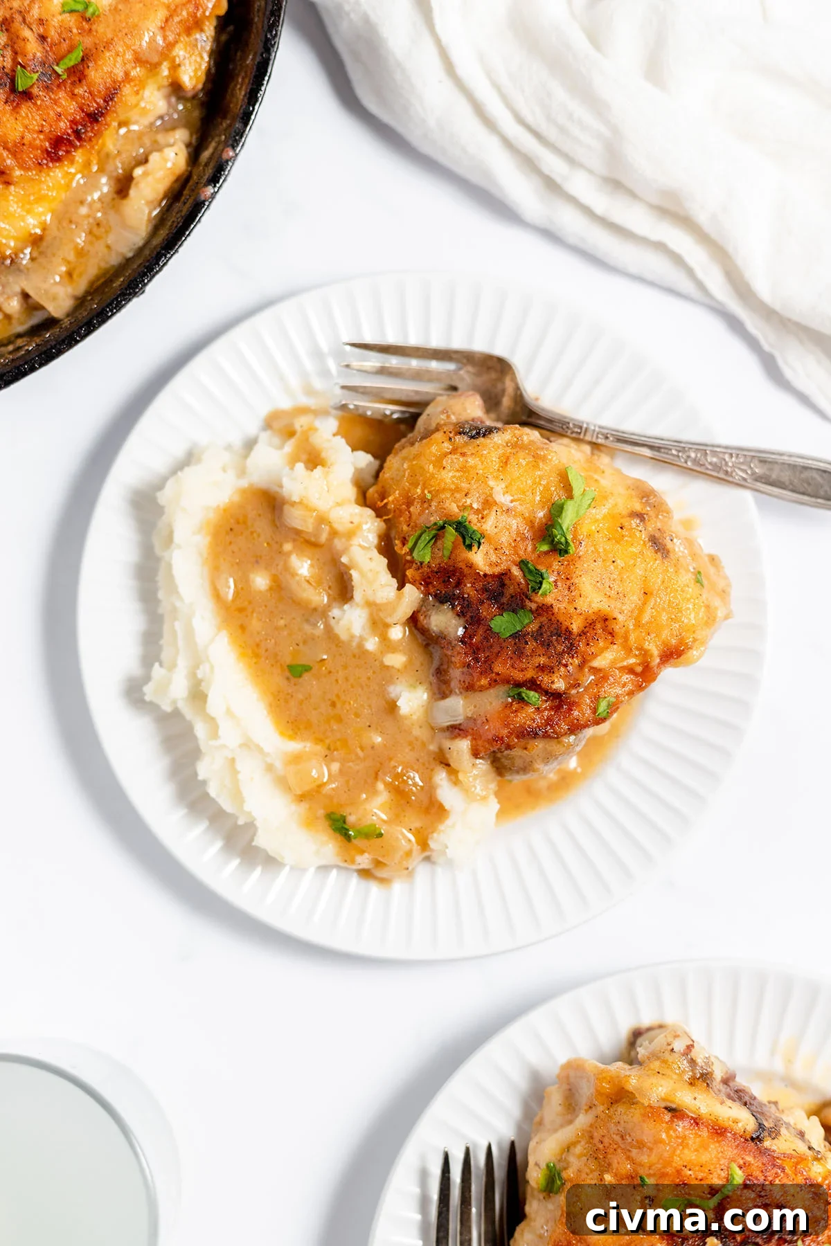 Smothered Chicken Thighs served on a plate with mashed potatoes and gravy.