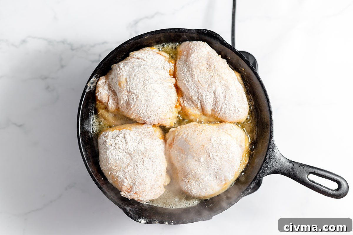 Chicken thighs are frying in a cast iron skillet.