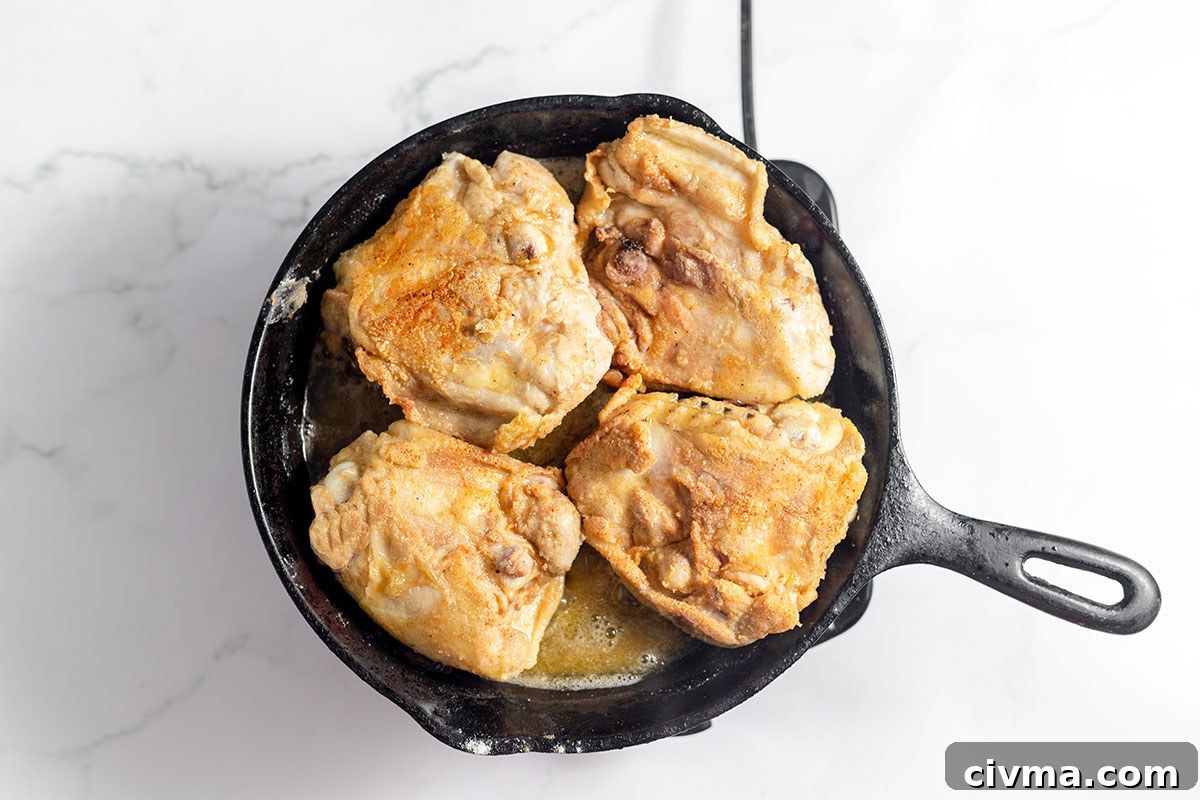 Chicken thighs browned in a cast iron skillet.