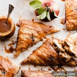 Puff pastry apple turnovers on a light surface with salted caramel sauce drizzled on and whole apples around.