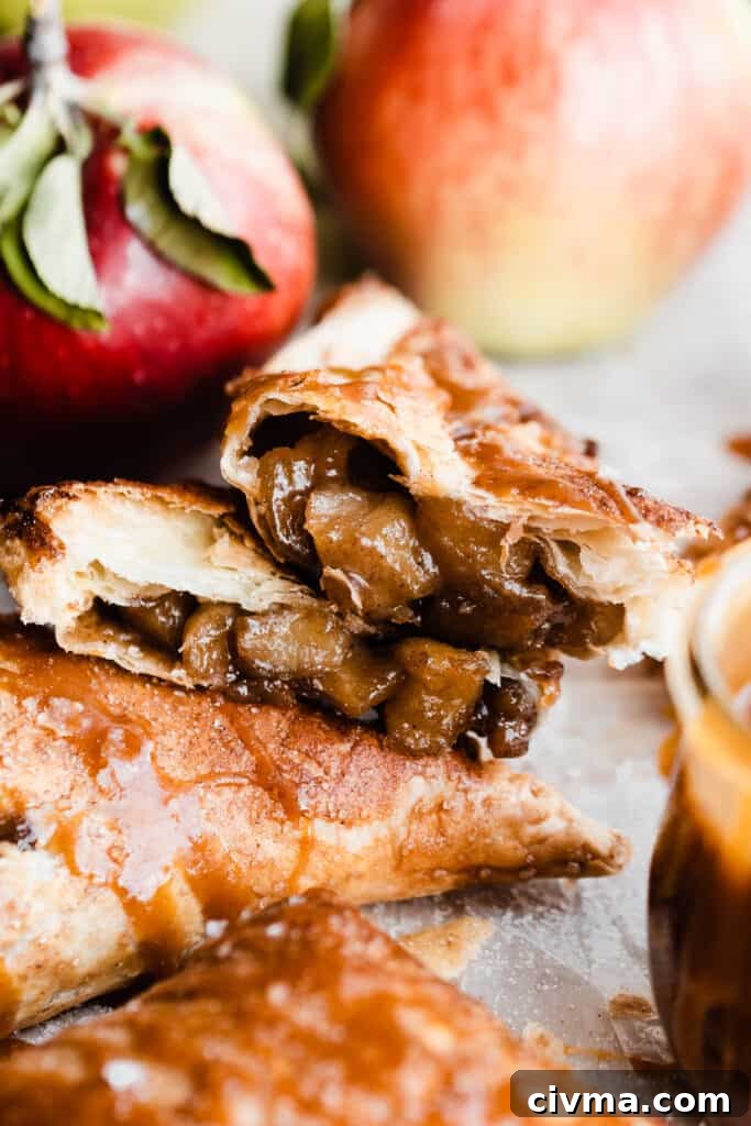 A close-up on the inside of a broken open turnover, with apple pie filling spilling out.
