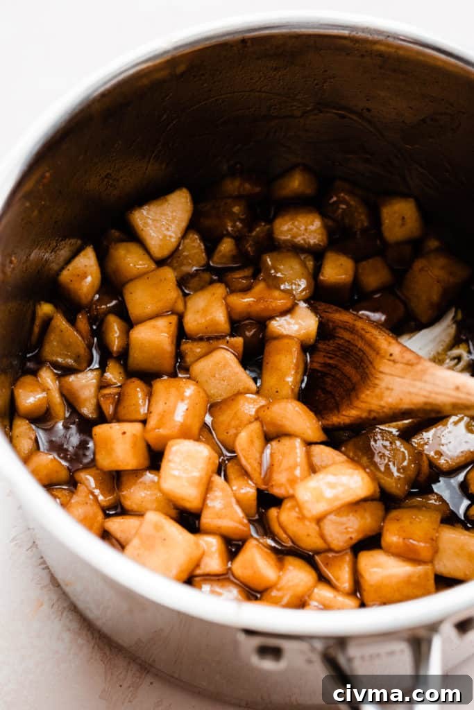 Cooked, golden apple filling in a pot, with a wooden spoon stirring the filling
