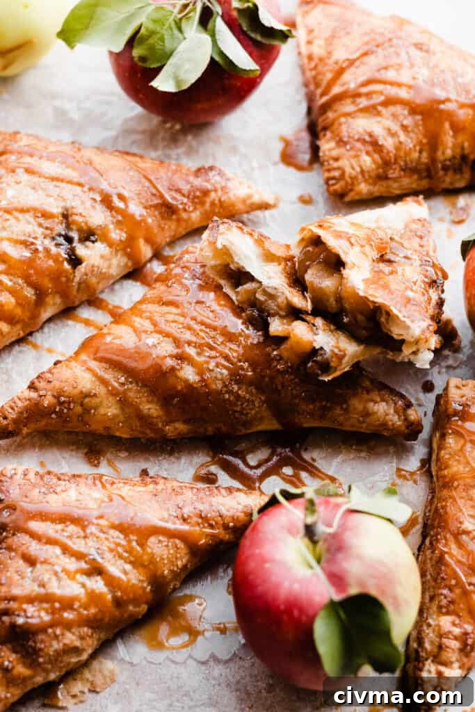 Apple turnovers drizzled with salted caramel sauce, with one broken open near some whole apples.