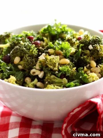 White bowl containing broccoli and kale salad with pine nuts and feta cheese on top, sitting on a red and white gingham napkin.