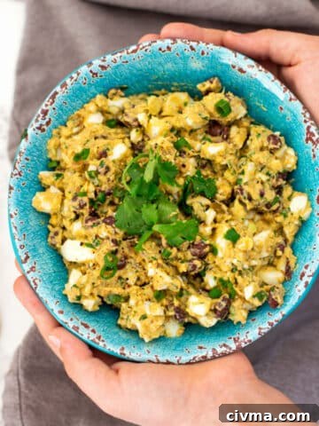 Turquoise bowl containing avocado egg salad, 2 hands holding bowl.