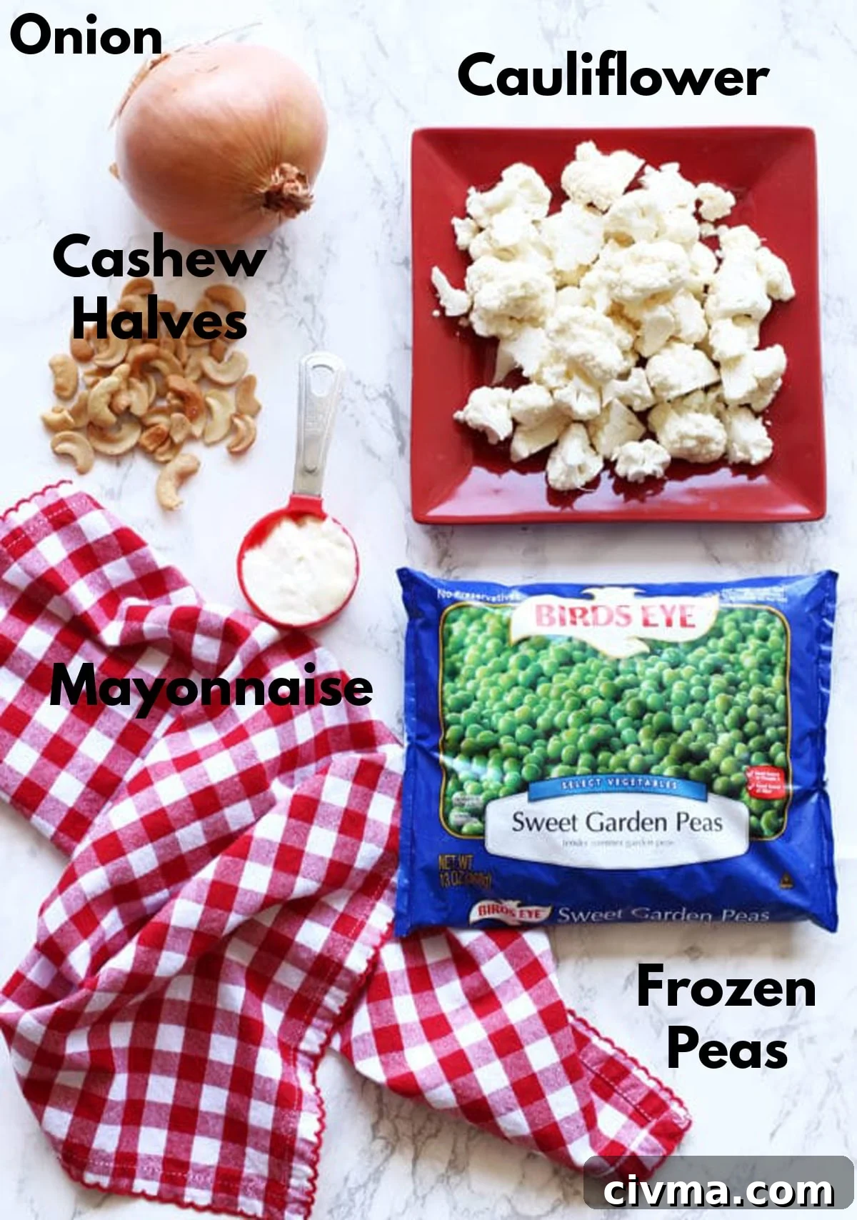 Cauliflower florets, onion, cashew halves, mayonnaise, and frozen peas on a marble countertop.