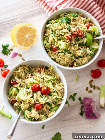 Two white bowls filled with an orzo pasta salad, lemon and tomatoes on table.