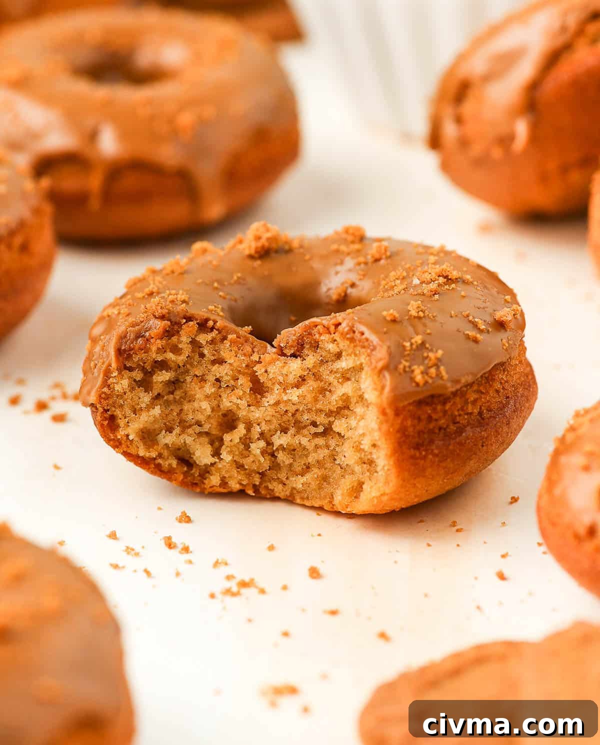 Biscoff Cookie Butter Donuts with Creamy Glaze 8 One bite taken off a cake on an orange surface.