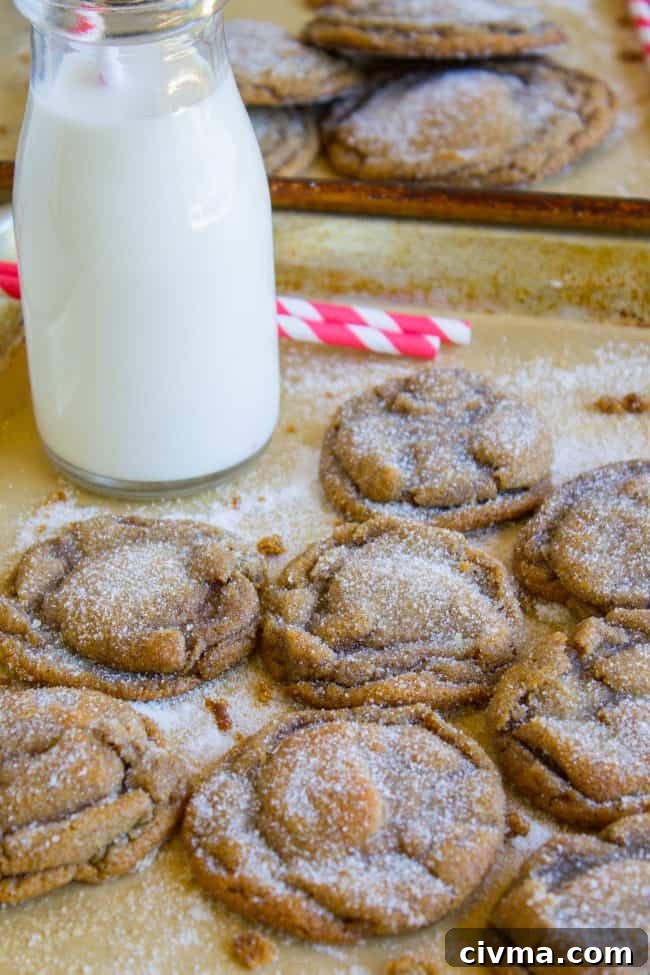 Molasses cookies cooling on cookie sheets with a bottle of milk and striped straws.
