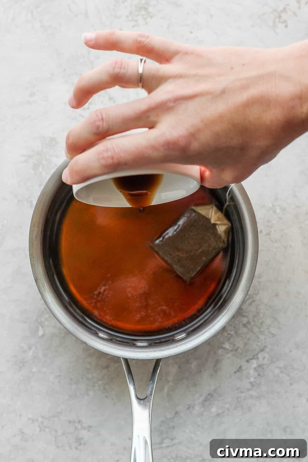 Adding maple syrup and vanilla to earl grey tea steeping in a small saucepan.