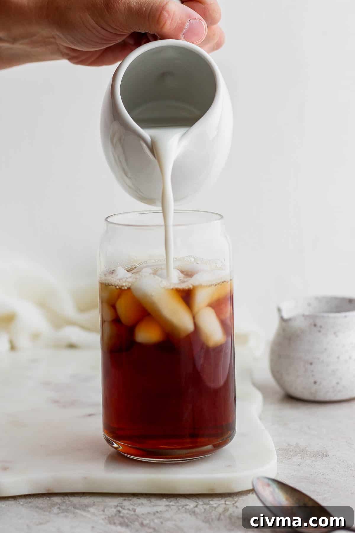Adding almond milk to a glass of iced early grey tea.