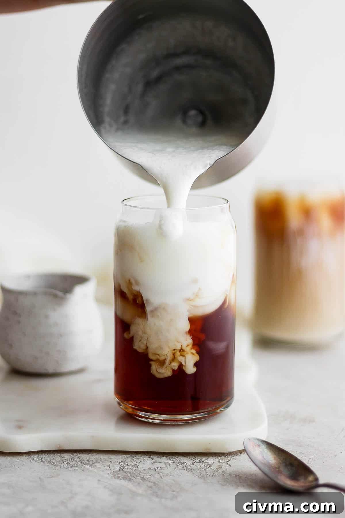 Adding frothed almond milk to a glass of iced early grey tea.
