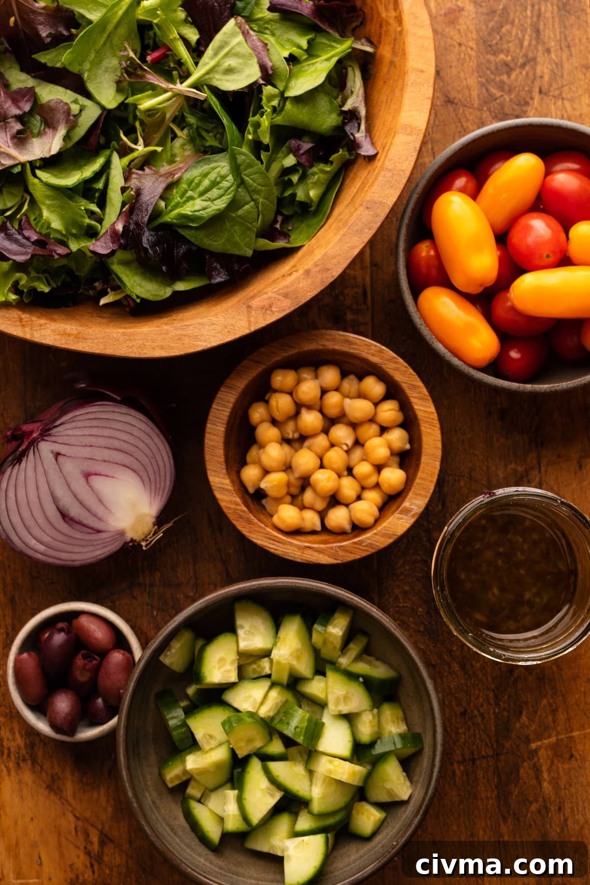 Ingredients for greek chickpea salad arranged in bowls on a wooden background.
