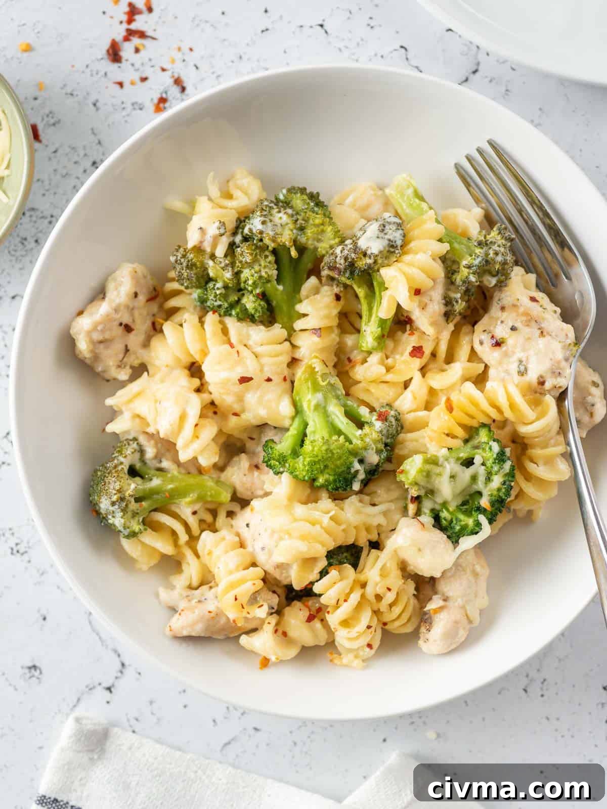 a fork placed on the side of the pasta and broccoli dish on a plate