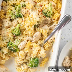 baked chicken and broccoli pasta in a white dish after baking with a spoon inside the dish