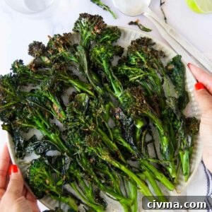 two hands with red nail polish hold a plate of air fryer broccolini after cooking