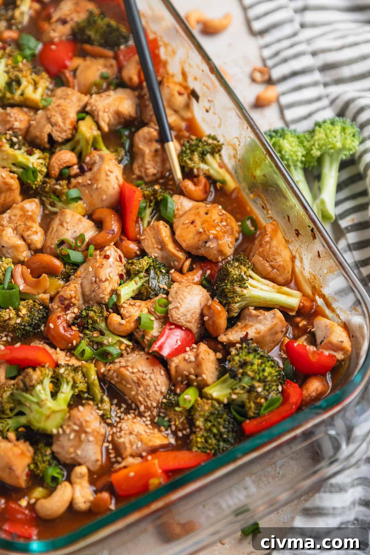 Glass baking pan with easy cashew chicken recipe and spoon scooping into it.