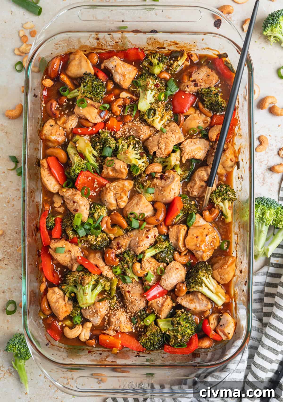 Baking pan with easy cashew chicken recipe in sauce and topped with sesame seeds and sliced scallions.
